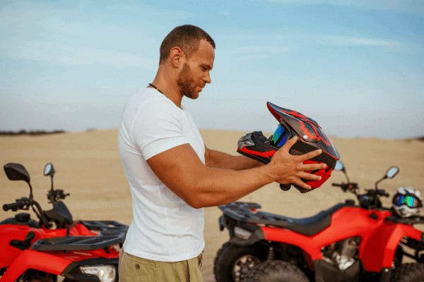 Man holding a motorcycle helmet outdoors. Morning Quad Bike Desert Safari